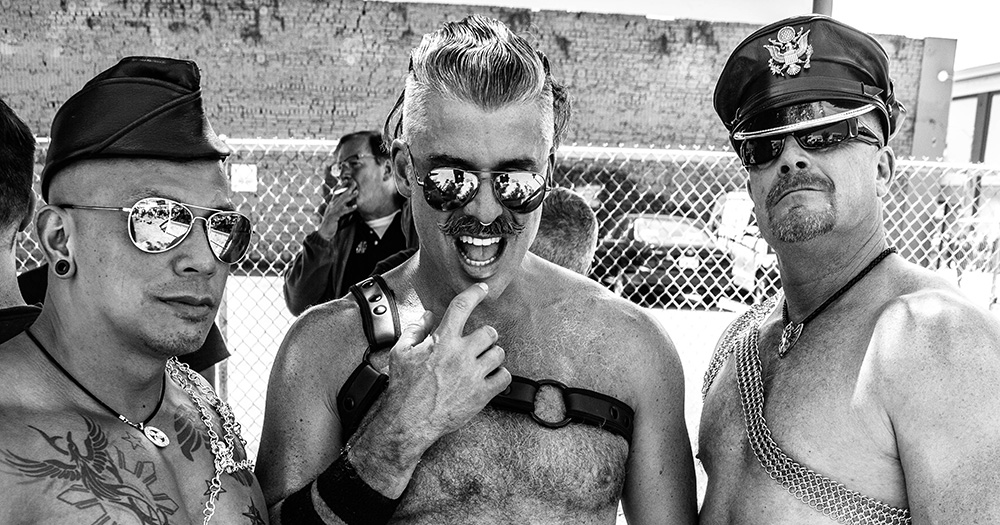 A black and white photo of three men at a fetish festival.