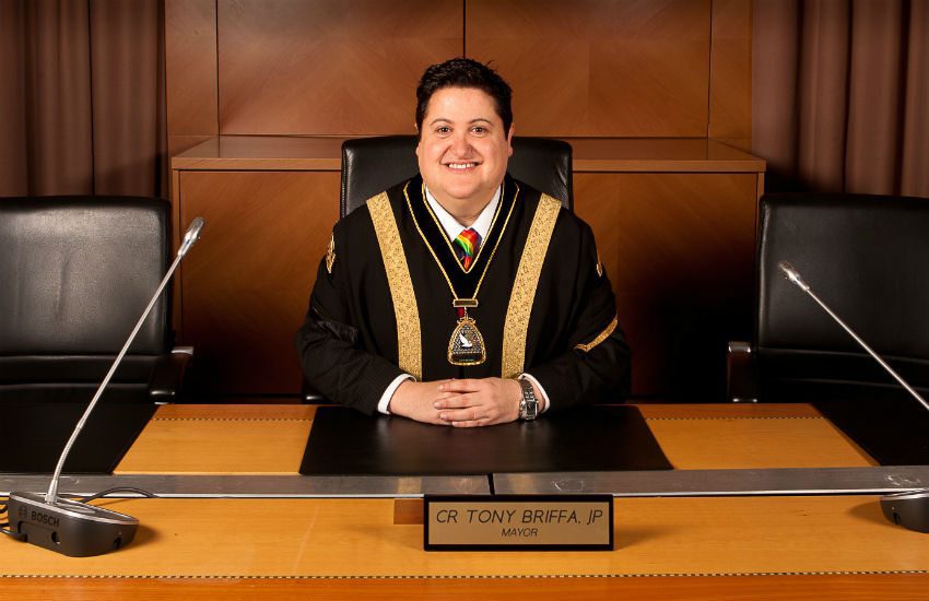 Tony Briffa wearing mayor robes and a rainbow tie at a government desk