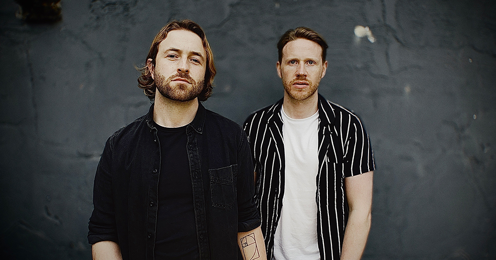 Musicians who are part of the band Phoeno, who has just released a new single, standing in front of a grey wall and looking at the camera.