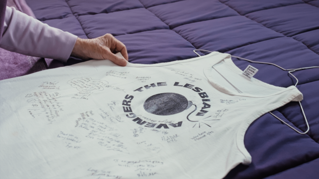 Edie Daly shows off ‘Lesbian Avengers’ shirt on a purple quilt.