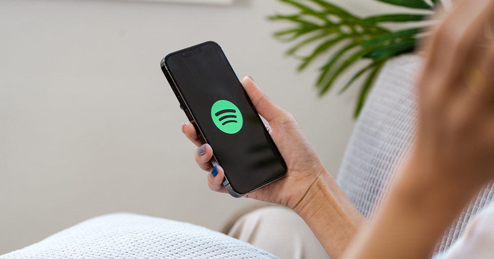 This article is about Spotify Wrapped 2024. In the photo, the hand of a person holding a phone with the Spotify logo on the screen.