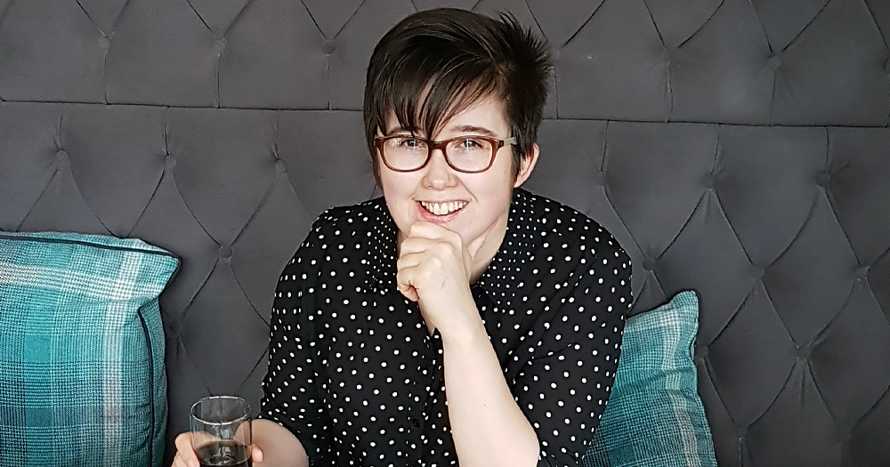 Photo Lyra McKee, with a bursary being launched in her name, sitting at a table while flipping to a newspaper and smiling at the camera.