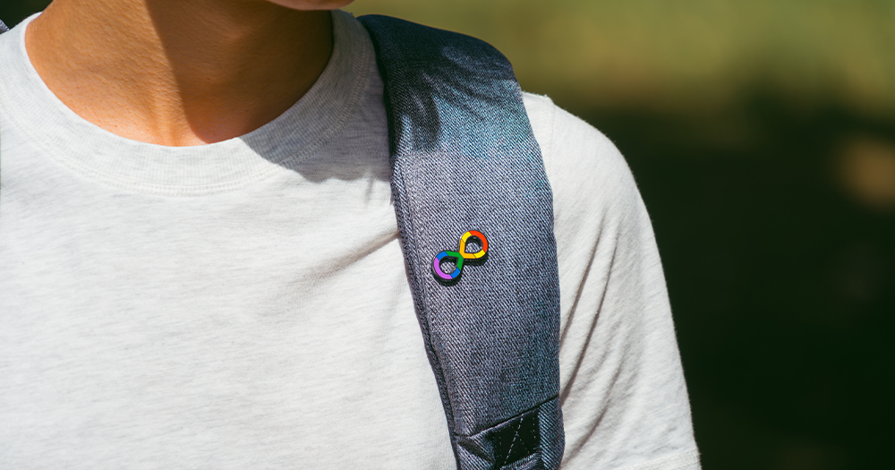 This article is about neurodivergent and queer people. In the photo, a person wearing an infinity rainbow pin.