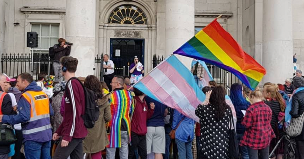 The image shows a pride and trans flag being held up infant of a government building. Vote with pride has responded to the upcoming governments programme