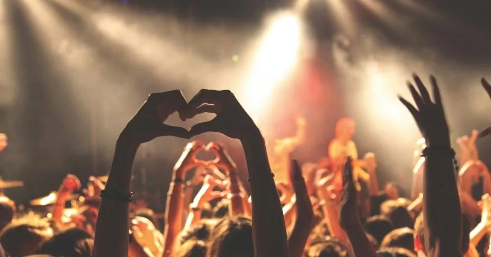 People in the crowd of a concert make heart shapes with their hands. This image is being used to represent the queer events taking place in Ireland in February.