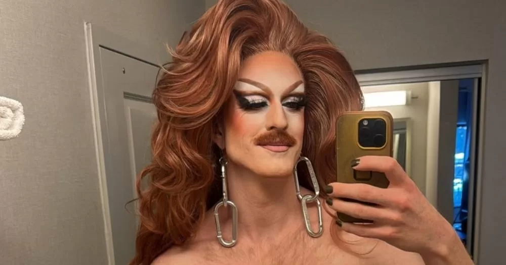 Drag queen Pattie Gonia taking a mirror selfie in full glamour. She is topless.
