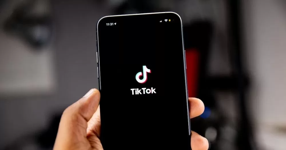 This article is about TikTok US collective sensitive information. In the photo, a hand holding a phone with the TikTok logo on the screen.