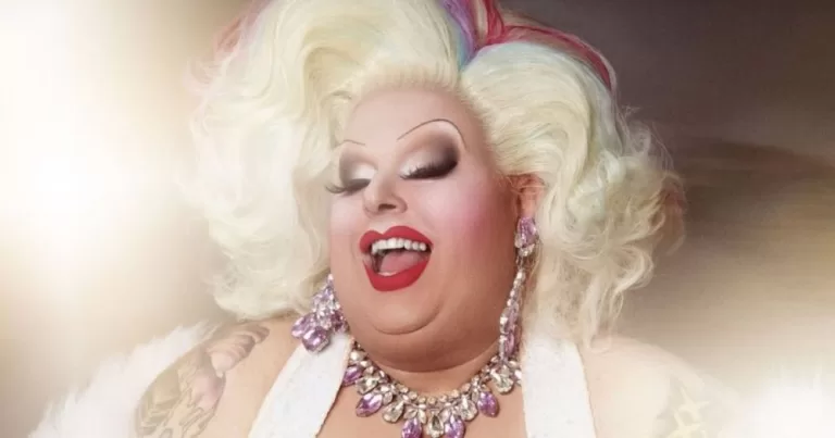 Maxi Shield poses in a white dress and a blonde qig.