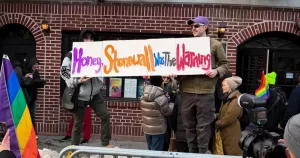 Image shows a protest sign being held by two people outside Stonewall. the protest was in response to the removal of the sites Pride flag. The sign reads " Honey, Stonewall was the warning"
