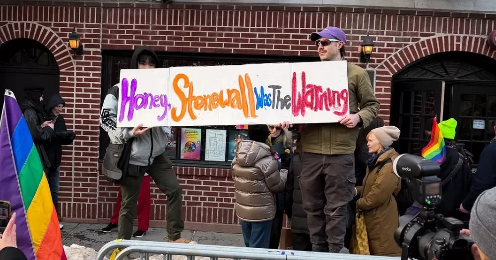 Image shows a protest sign being held by two people outside Stonewall. the protest was in response to the removal of the sites Pride flag. The sign reads " Honey, Stonewall was the warning"