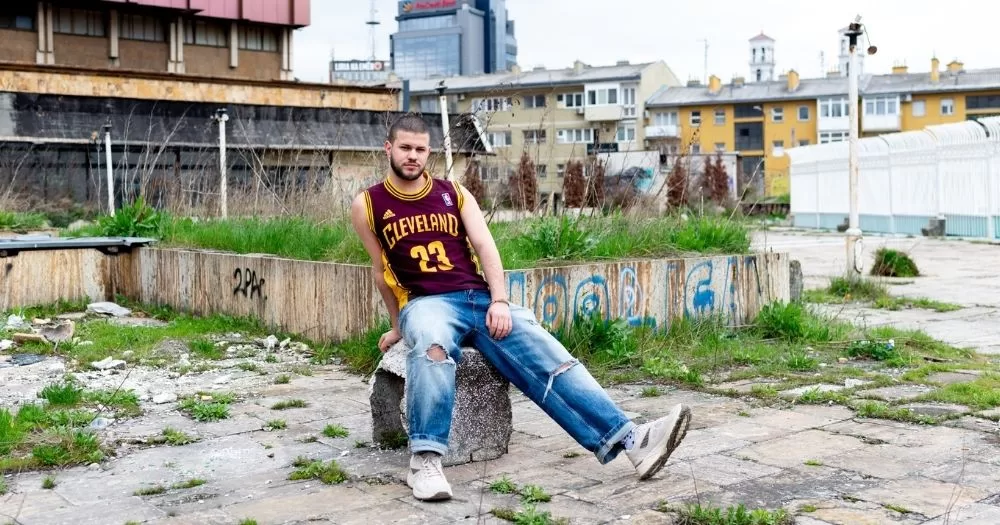 A man sits on a concrete block in a Balkan city.