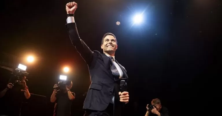 Rob Jetten, who became The Netherlands' first gay Prime Minister, holding a microphone on a stage with his fist raised in victory.